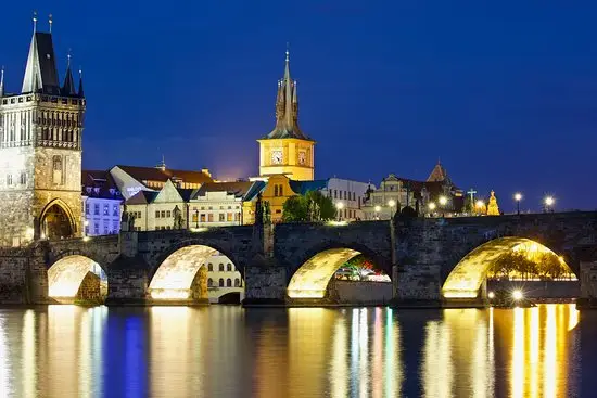 Noční Karlův most s lucernami, odrazy světel na Vltavě